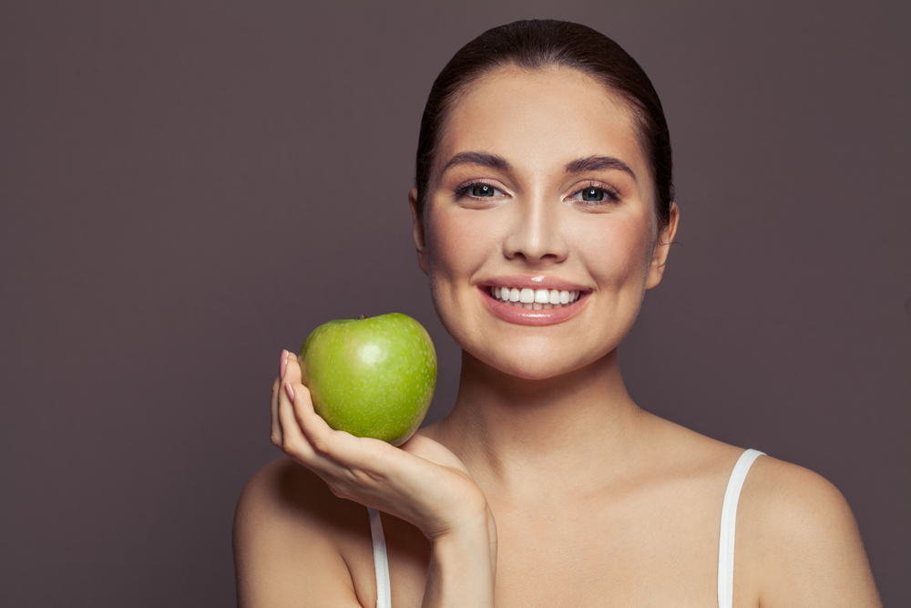Woman holding an apple while smiling.